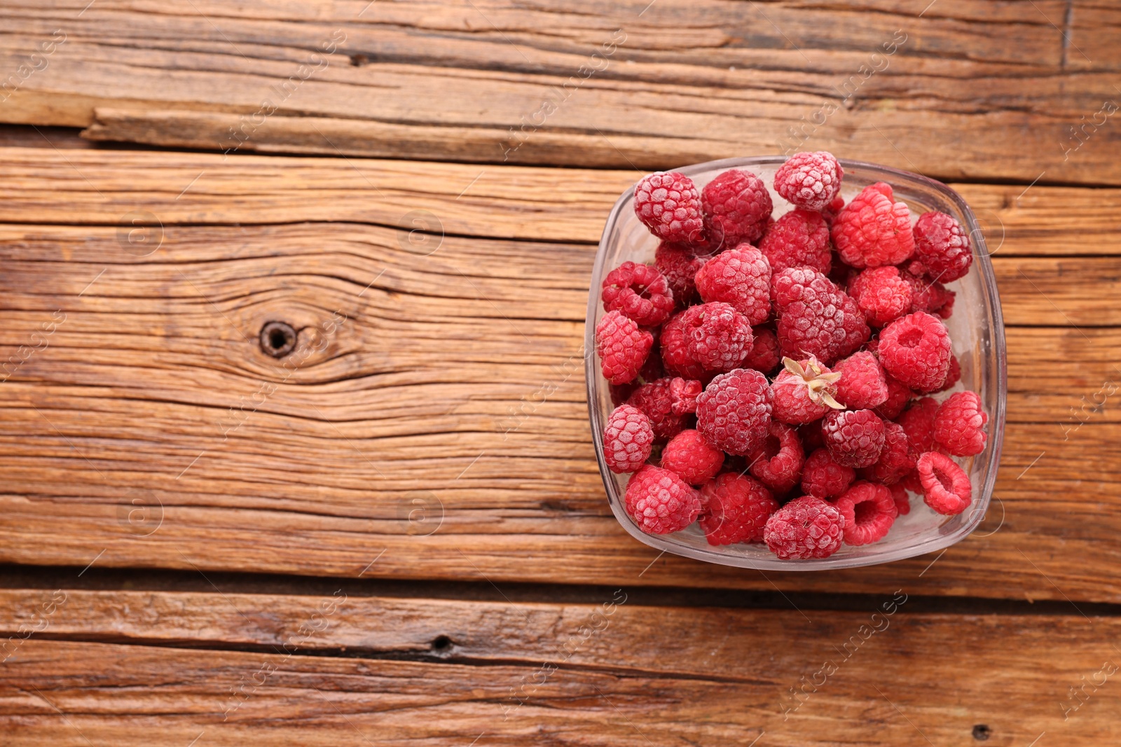 Photo of Ripe frozen raspberries in bowl on wooden table, top view. Space for text