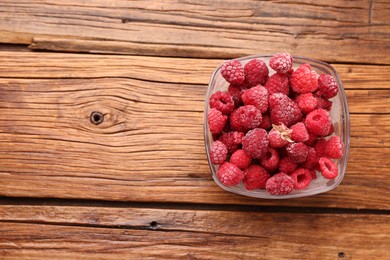 Photo of Ripe frozen raspberries in bowl on wooden table, top view. Space for text