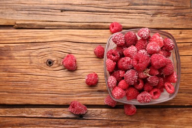 Photo of Ripe frozen raspberries in bowl on wooden table, flat lay. Space for text