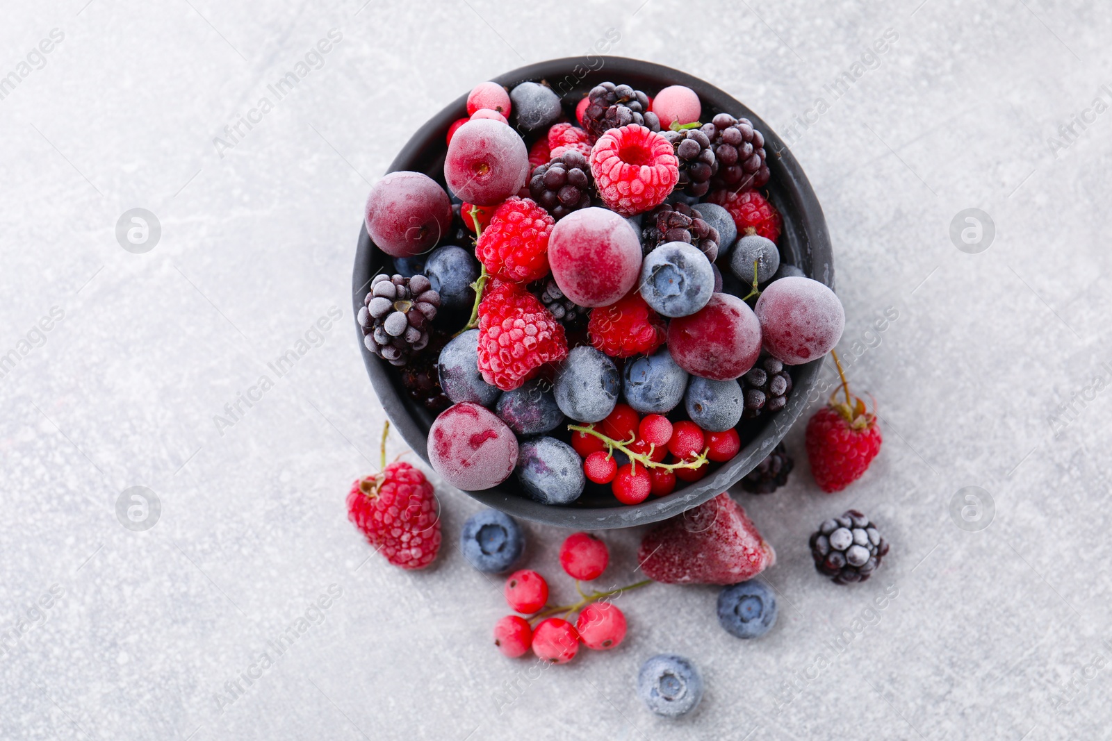 Photo of Mix of ripe frozen berries and bowl on grey textured table, flat lay