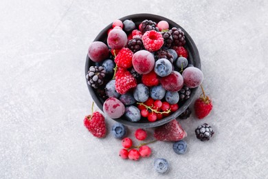 Photo of Mix of ripe frozen berries and bowl on grey textured table, flat lay