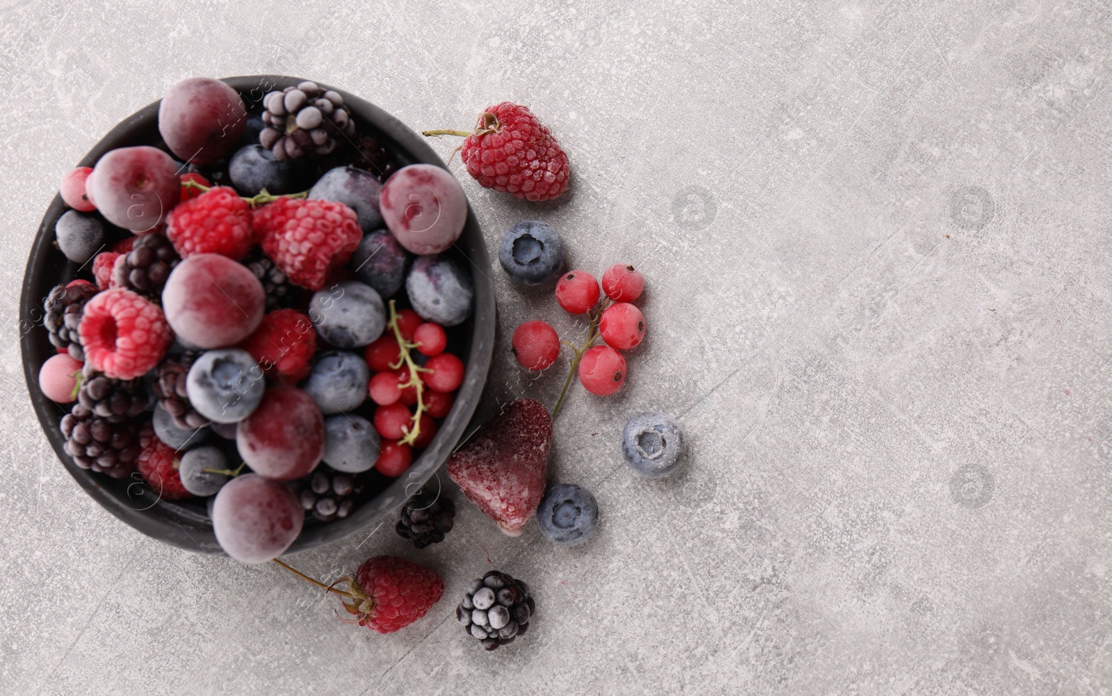 Photo of Mix of ripe frozen berries and bowl on grey textured table, flat lay. Space for text