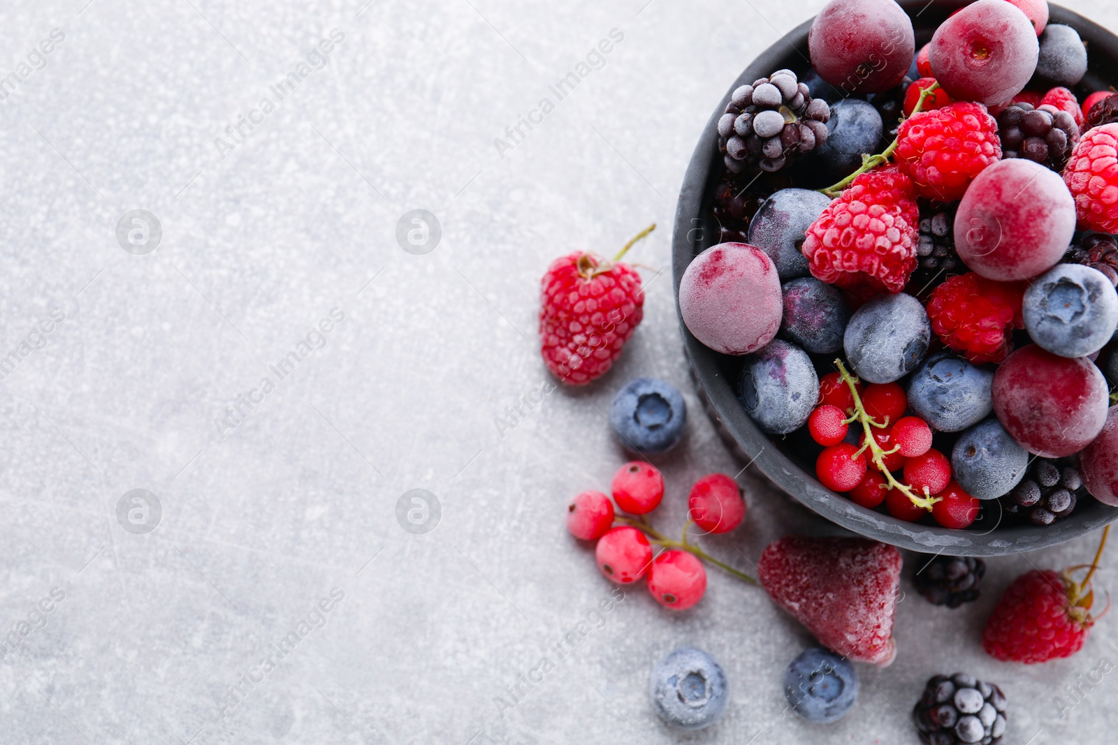 Photo of Mix of ripe frozen berries and bowl on grey textured table, flat lay. Space for text