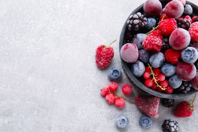 Photo of Mix of ripe frozen berries and bowl on grey textured table, flat lay. Space for text