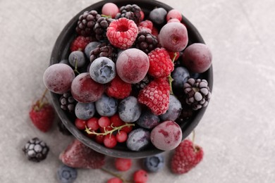 Photo of Mix of ripe frozen berries and bowl on grey textured table, flat lay