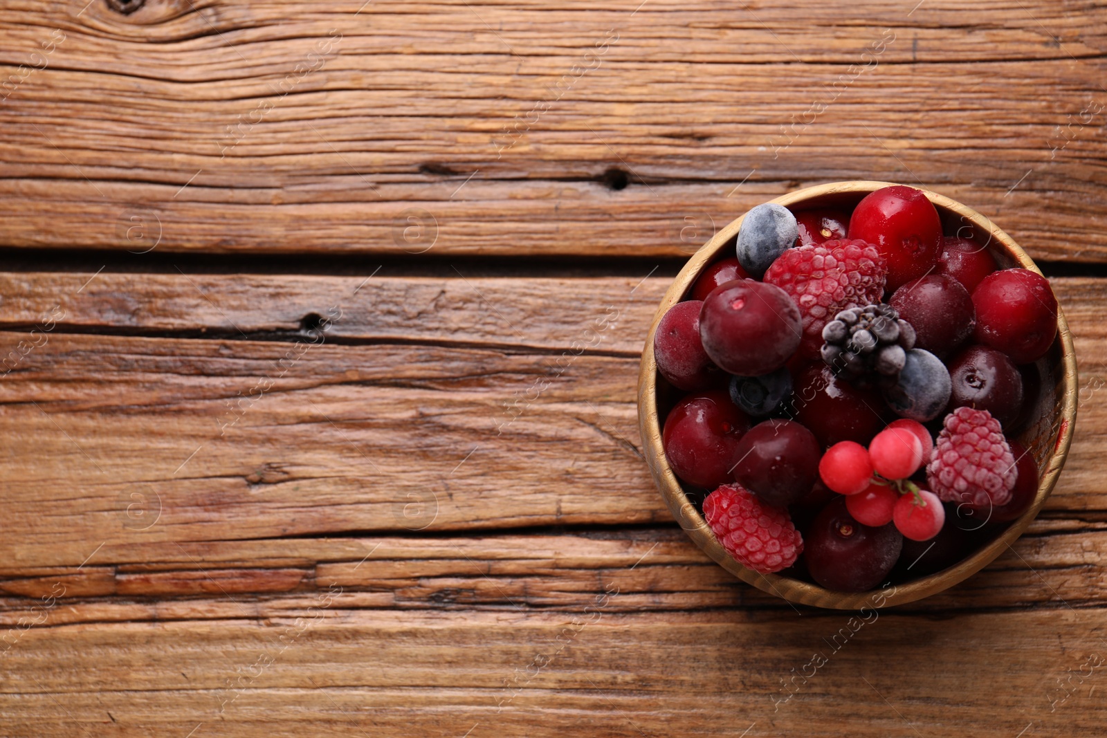 Photo of Mix of ripe frozen berries in bowl on wooden table, top view. Space for text
