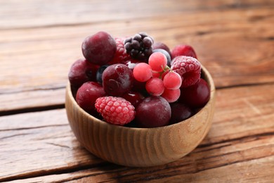 Photo of Mix of ripe frozen berries in bowl on wooden table, closeup
