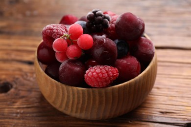 Photo of Mix of ripe frozen berries in bowl on wooden table, closeup