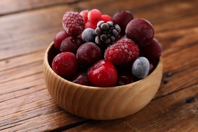 Photo of Mix of ripe frozen berries in bowl on wooden table, closeup