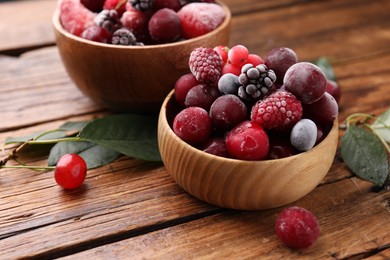 Photo of Mix of ripe frozen berries and green leaves on wooden table, closeup