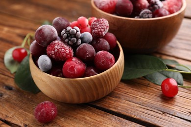 Photo of Mix of ripe frozen berries and green leaves on wooden table, closeup