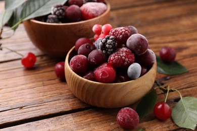 Photo of Mix of ripe frozen berries and green leaves on wooden table, closeup