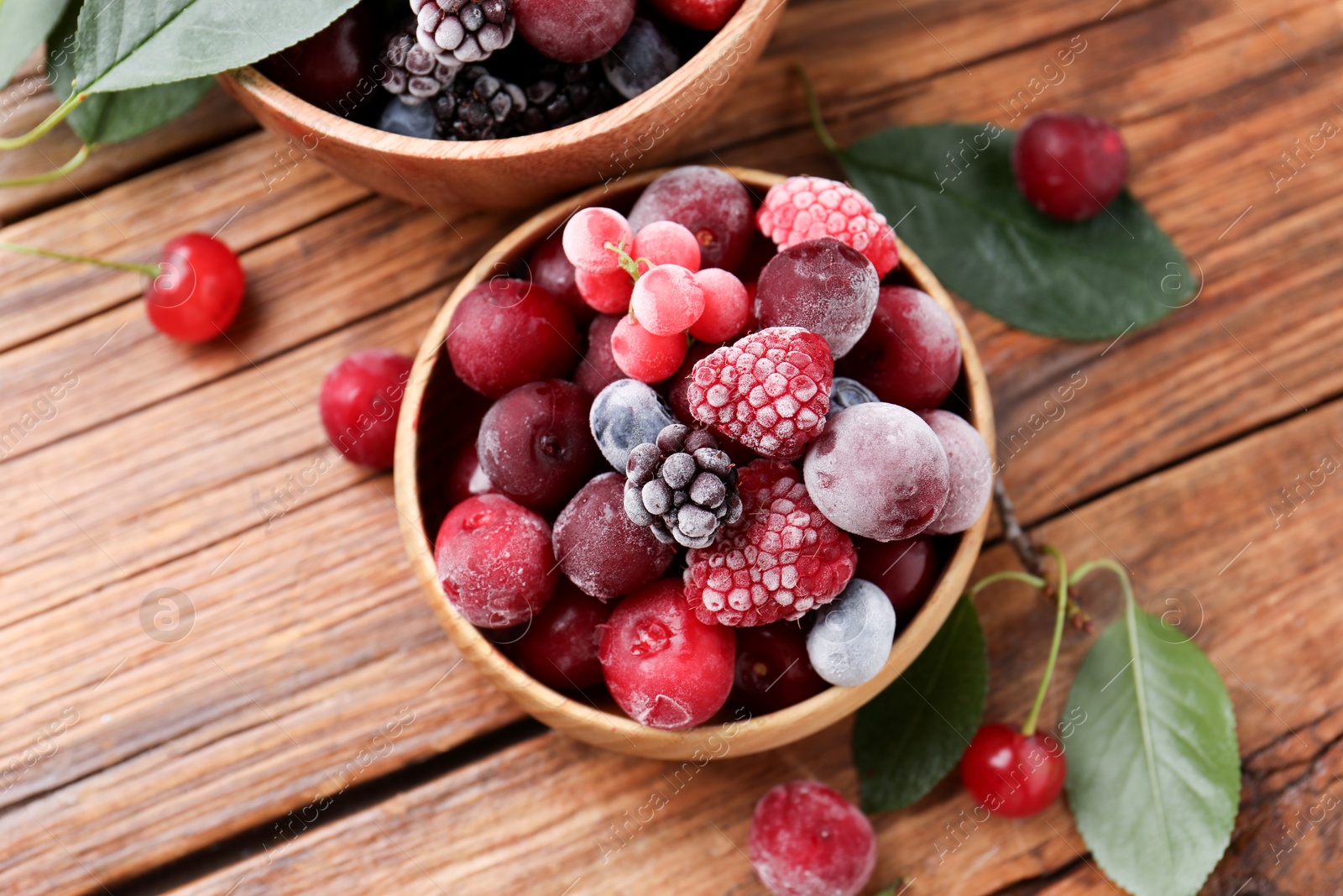 Photo of Mix of ripe frozen berries and green leaves on wooden table, flat lay