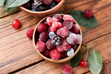 Photo of Mix of ripe frozen berries and green leaves on wooden table, flat lay