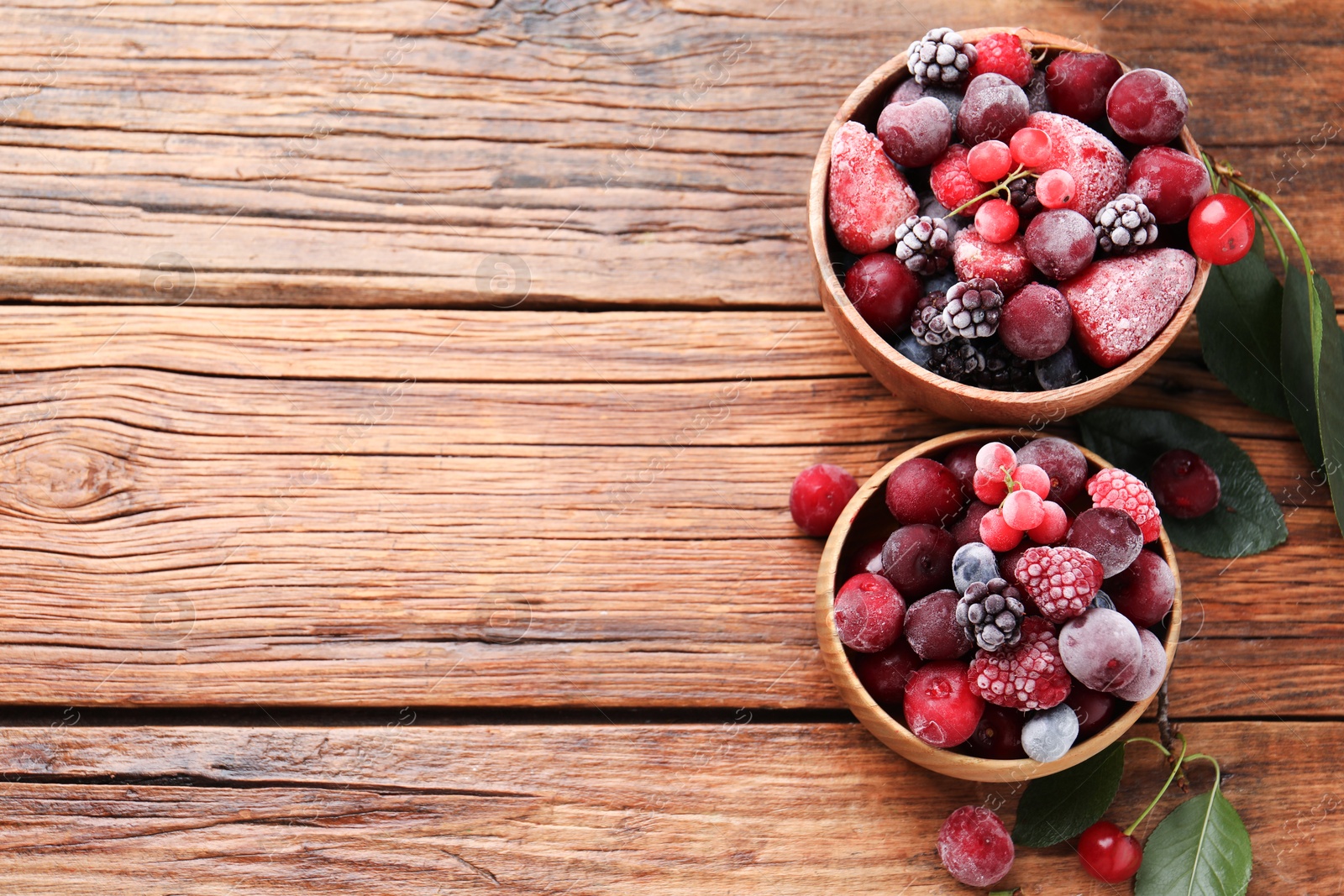 Photo of Mix of ripe frozen berries and green leaves on wooden table, flat lay. Space for text
