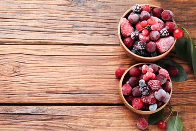 Photo of Mix of ripe frozen berries and green leaves on wooden table, flat lay. Space for text