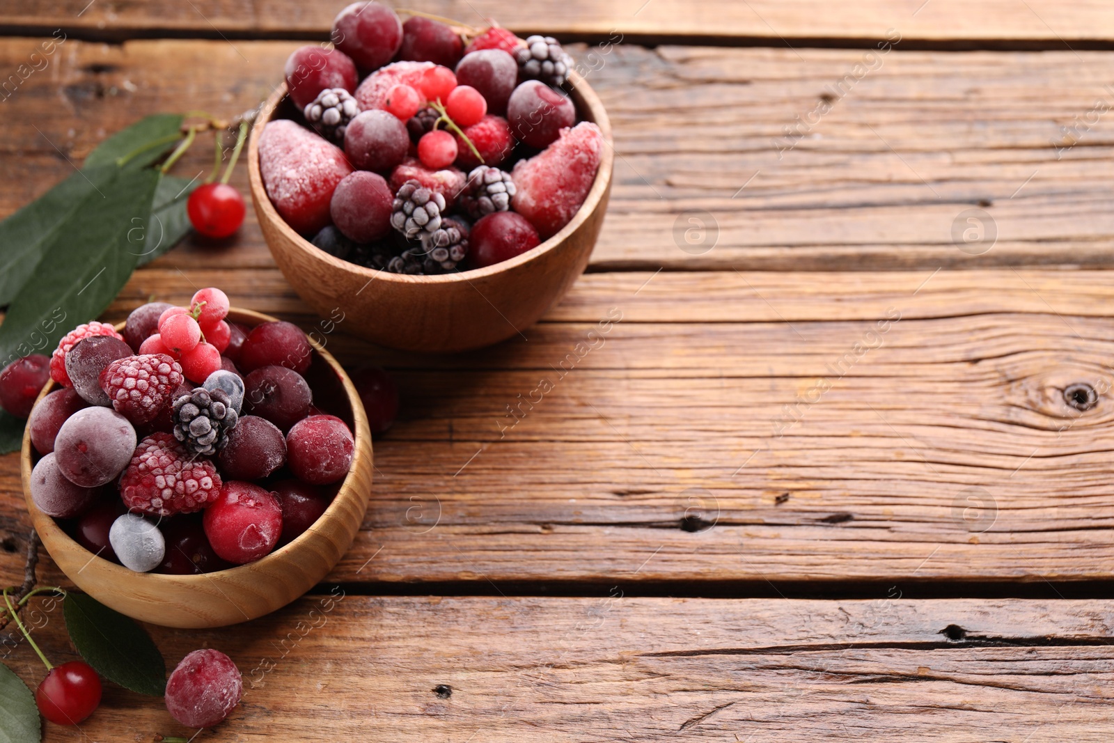 Photo of Mix of ripe frozen berries and green leaves on wooden table, closeup. Space for text