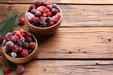 Photo of Mix of ripe frozen berries and green leaves on wooden table, closeup. Space for text