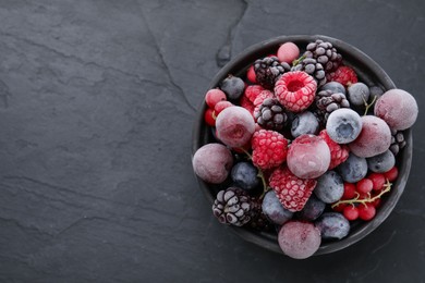 Photo of Mix of ripe frozen berries in bowl on dark textured table, top view. Space for text