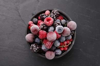 Photo of Mix of ripe frozen berries in bowl on dark textured table, top view