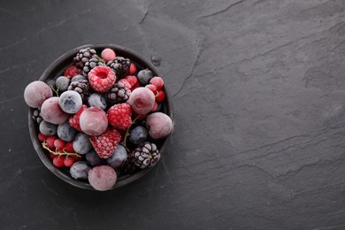 Photo of Mix of ripe frozen berries in bowl on dark textured table, top view. Space for text
