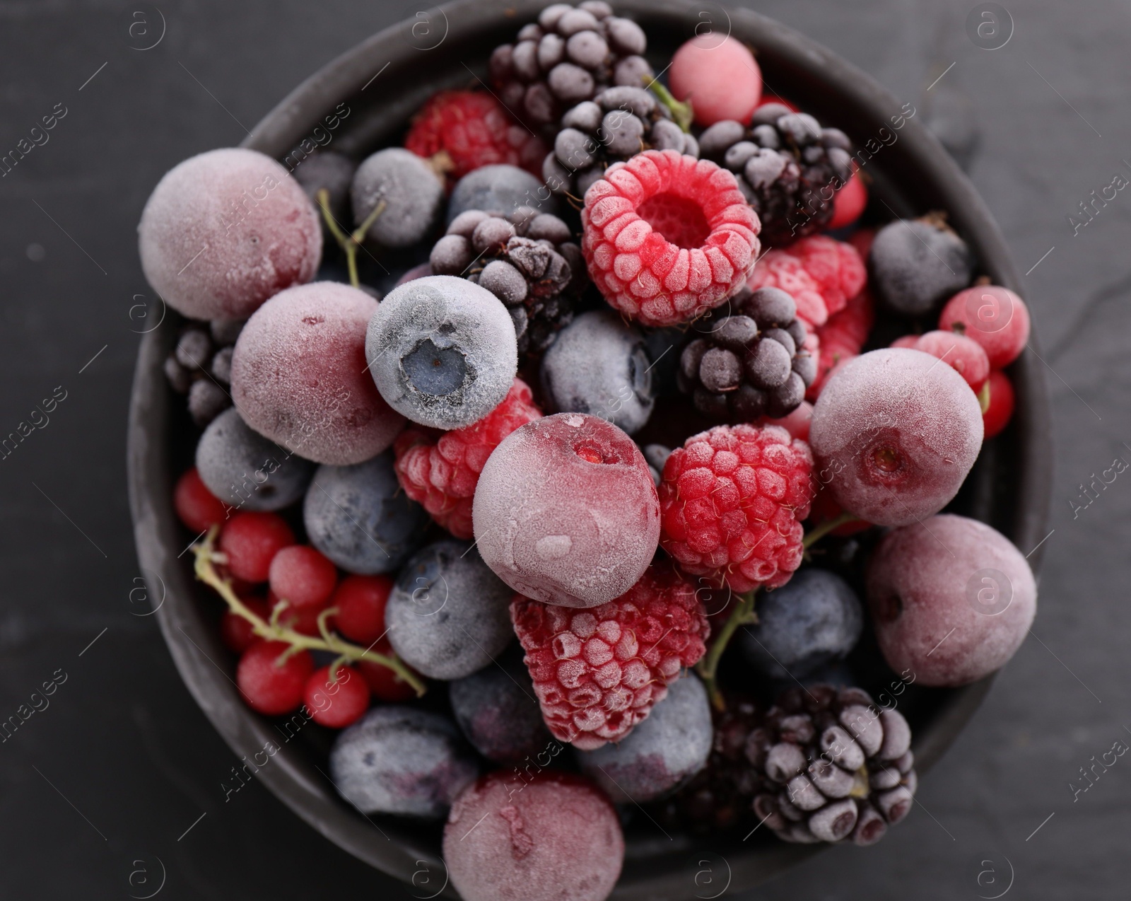 Photo of Mix of ripe frozen berries in bowl on dark textured table, top view