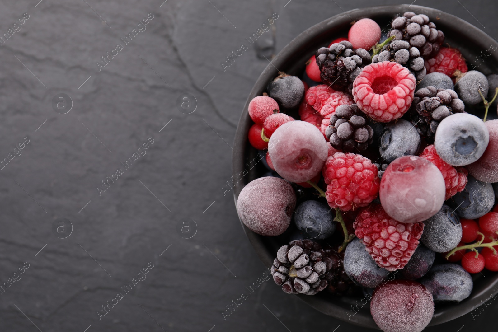 Photo of Mix of ripe frozen berries in bowl on dark textured table, top view. Space for text