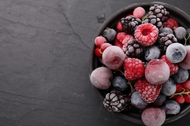 Photo of Mix of ripe frozen berries in bowl on dark textured table, top view. Space for text