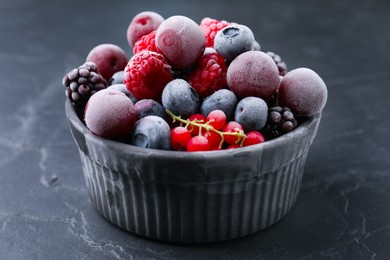 Photo of Mix of ripe frozen berries in bowl on dark textured table, closeup