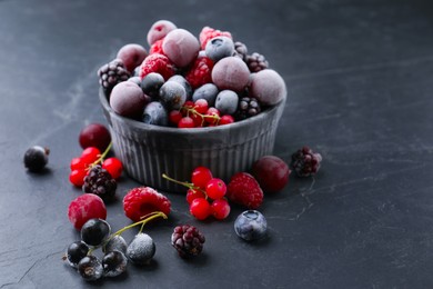 Photo of Mix of ripe frozen berries and bowl on dark textured table, closeup