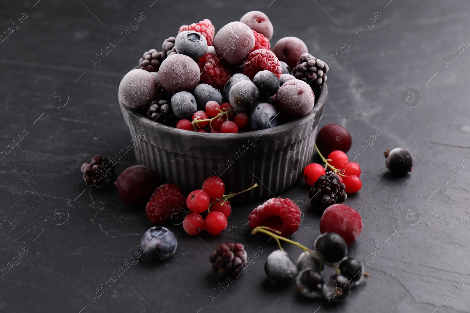 Photo of Mix of ripe frozen berries and bowl on dark textured table, closeup