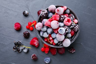 Photo of Mix of ripe frozen berries and bowl on dark textured table, flat lay