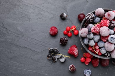 Photo of Mix of ripe frozen berries and bowl on dark textured table, flat lay. Space for text
