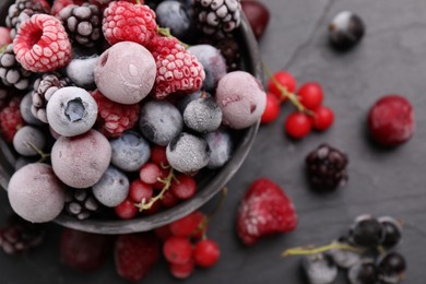 Photo of Mix of ripe frozen berries and bowl on dark textured table, flat lay