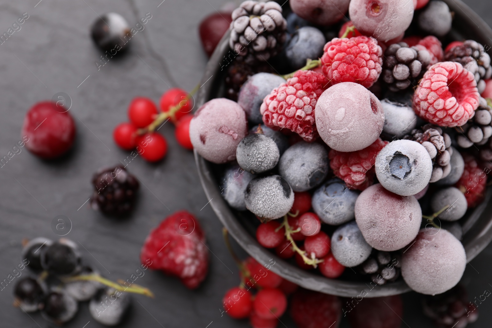 Photo of Mix of ripe frozen berries and bowl on dark textured table, flat lay
