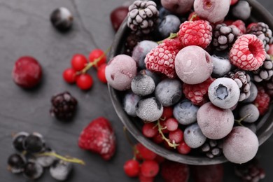 Photo of Mix of ripe frozen berries and bowl on dark textured table, flat lay
