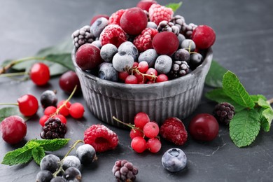 Photo of Mix of ripe frozen berries, mint leaves and bowl on dark textured table, closeup