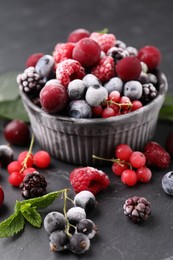 Photo of Mix of ripe frozen berries, mint leaves and bowl on dark textured table, closeup