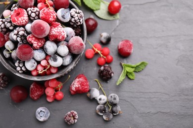 Photo of Mix of ripe frozen berries, mint leaves and bowl on dark textured table, flat lay. Space for text