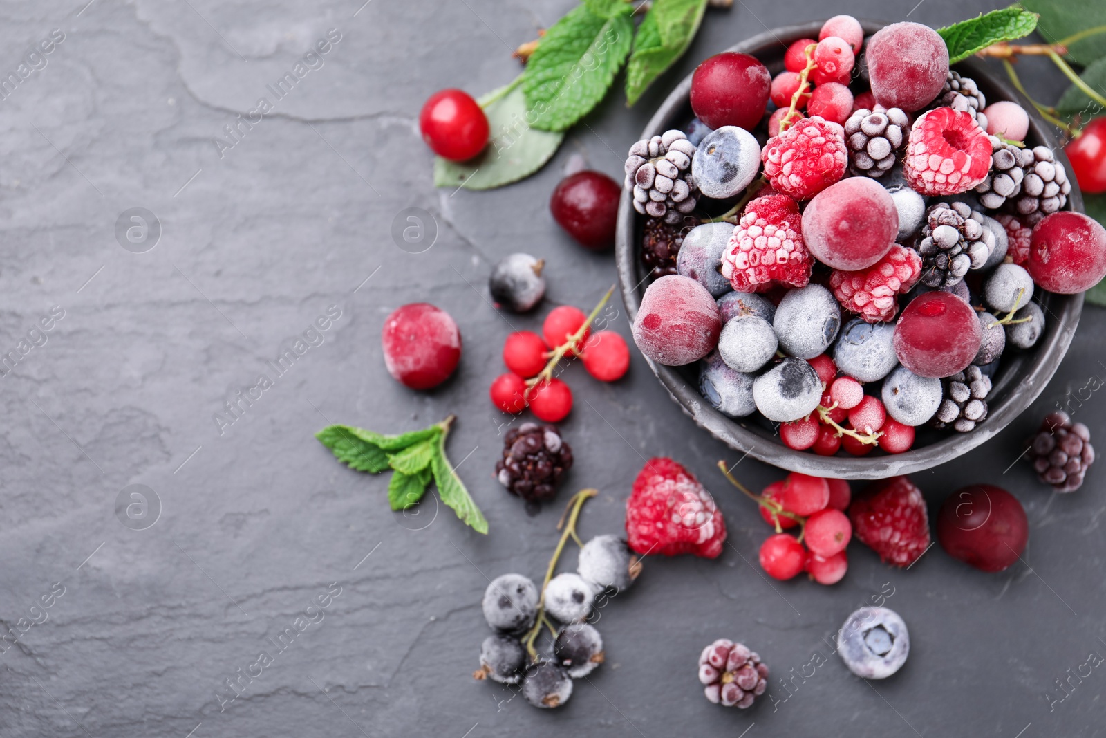 Photo of Mix of ripe frozen berries, mint leaves and bowl on dark textured table, flat lay. Space for text