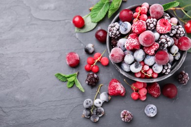 Photo of Mix of ripe frozen berries, mint leaves and bowl on dark textured table, flat lay. Space for text