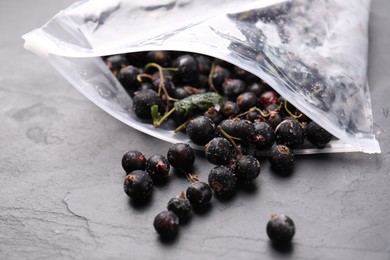 Photo of Ripe frozen black currants and open plastic bag on grey textured table, closeup