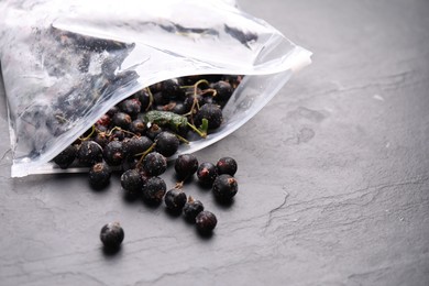 Photo of Ripe frozen black currants and open plastic bag on grey textured table, closeup