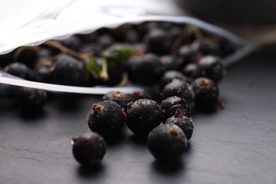 Photo of Ripe frozen black currants and open plastic bag on grey textured table, closeup