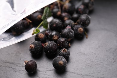 Photo of Ripe frozen black currants and open plastic bag on grey textured table, closeup