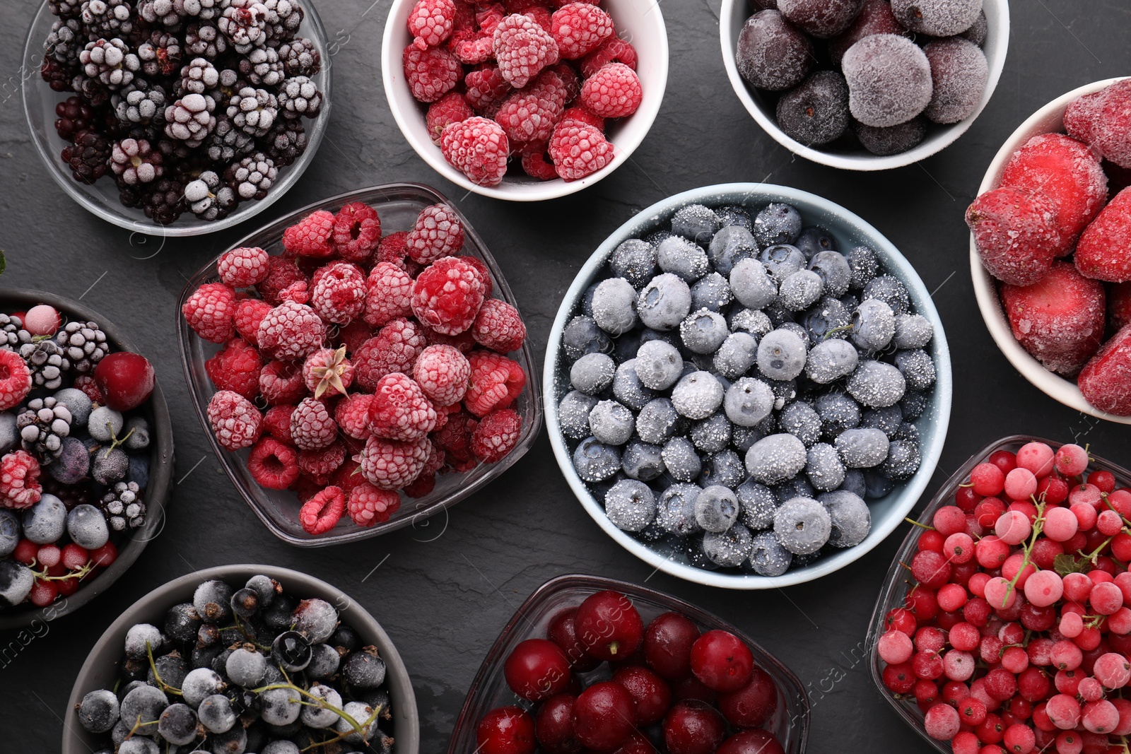 Photo of Different ripe frozen berries in bowls on dark textured table, flat lay