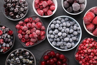 Photo of Different ripe frozen berries in bowls on dark textured table, flat lay