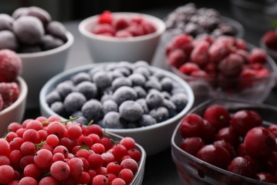 Photo of Different ripe frozen berries in bowls on table against black background, closeup