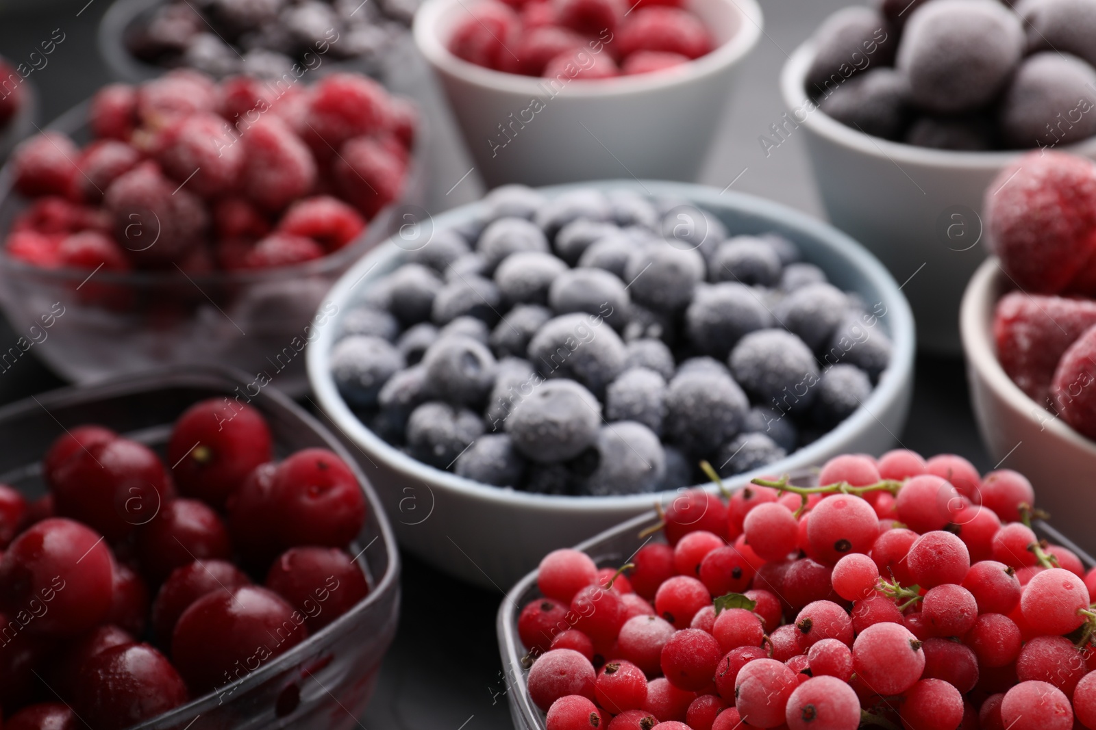 Photo of Different ripe frozen berries in bowls on grey table, closeup