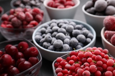 Photo of Different ripe frozen berries in bowls on grey table, closeup